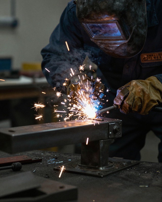 A welder joining steel, sparks scattering across the bench.