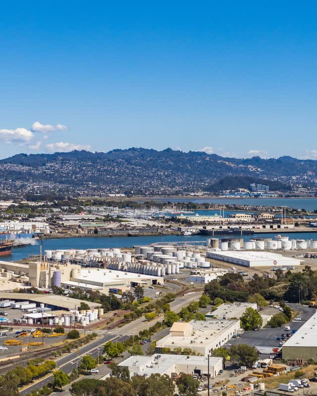 Warehouses and rail lines along the Oakland waterfront with hills beyond.